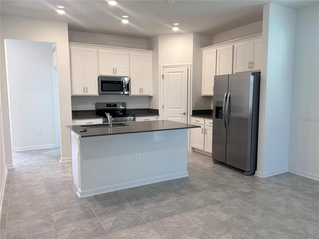 A kitchen features white cabinets, stainless steel appliances, a dark countertop island, and gray tile flooring — 6110 BLISSFUL STREET, CLERMONT, FL