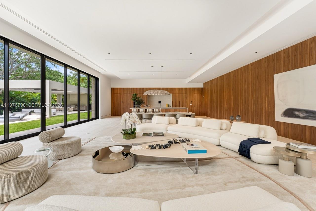 A spacious living room features white sofas, wood-paneled walls, and floor-to-ceiling glass doors — 8755 SW 54th Ave, Miami FL 33143, MIAMI, FL