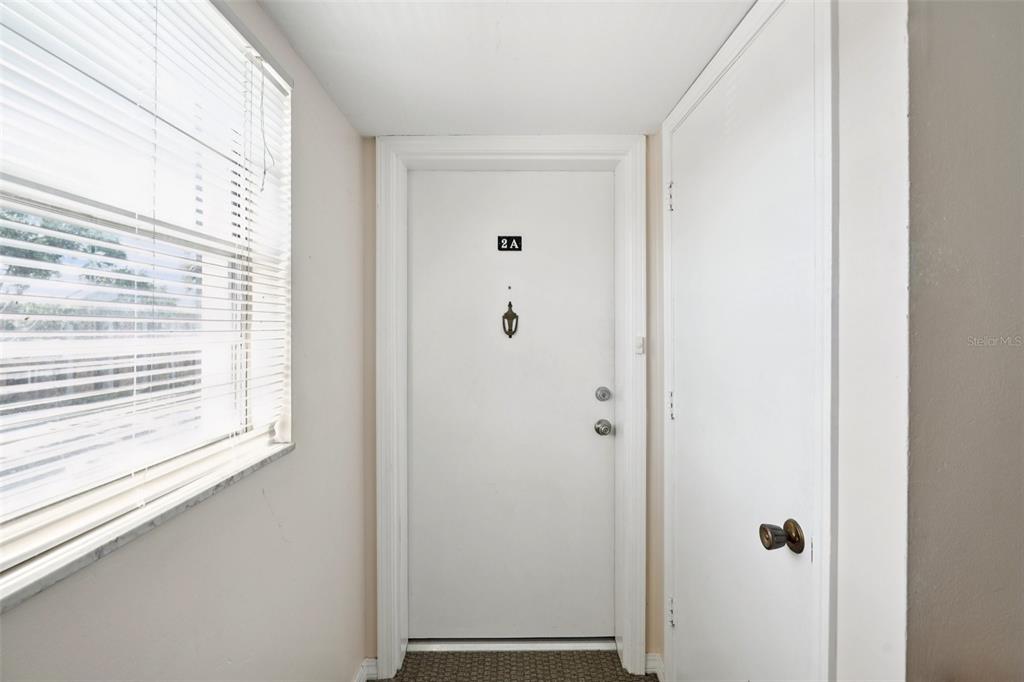 A white front door labeled 2A sits between a window with blinds and a closet — 1115 RUE DES CHATEAUX UNIT 2A, SOUTH PASADENA, FL