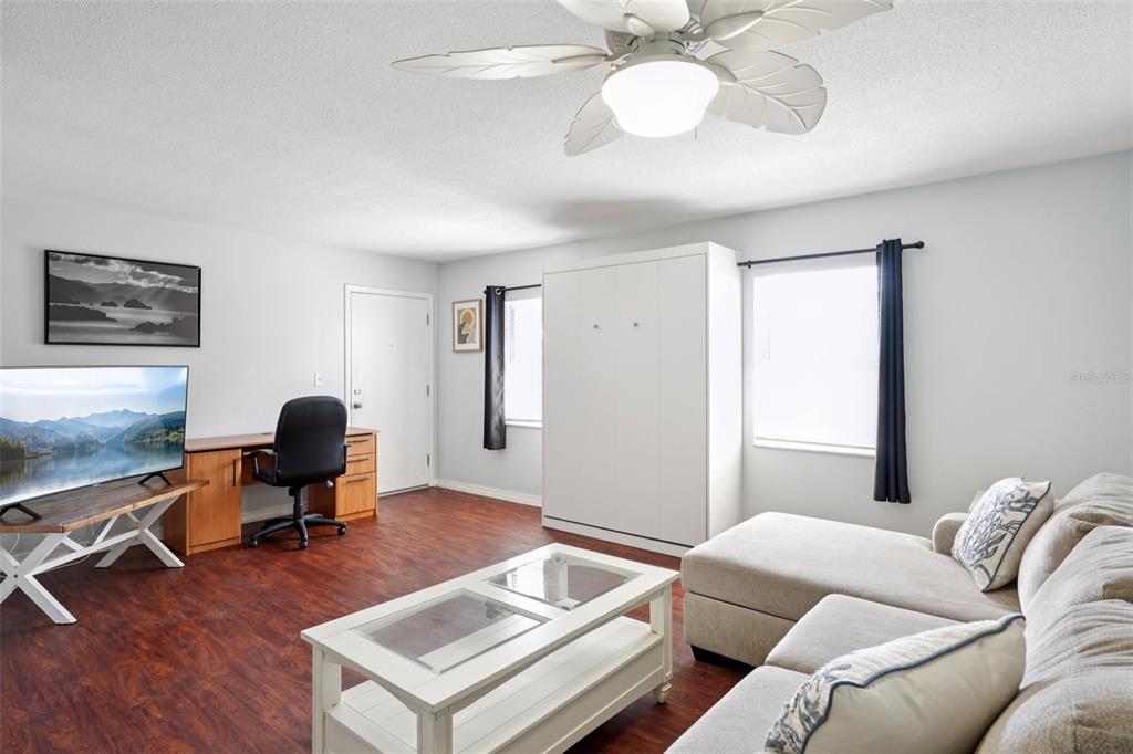 A living room features a white Murphy bed, a desk, a sofa, and wood flooring — 1115 RUE DES CHATEAUX UNIT 2A, SOUTH PASADENA, FL