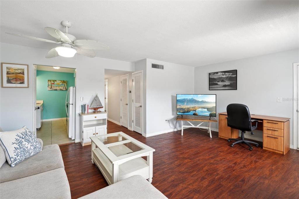 A living room features dark wood-look flooring, a ceiling fan, a desk, and a television — 1115 RUE DES CHATEAUX UNIT 2A, SOUTH PASADENA, FL