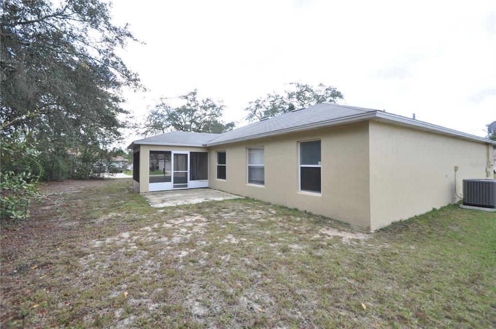 The exterior of a tan house features a screened-in porch and a concrete patio — 65 ROLLING FERN DRIVE, PALM COAST, FL