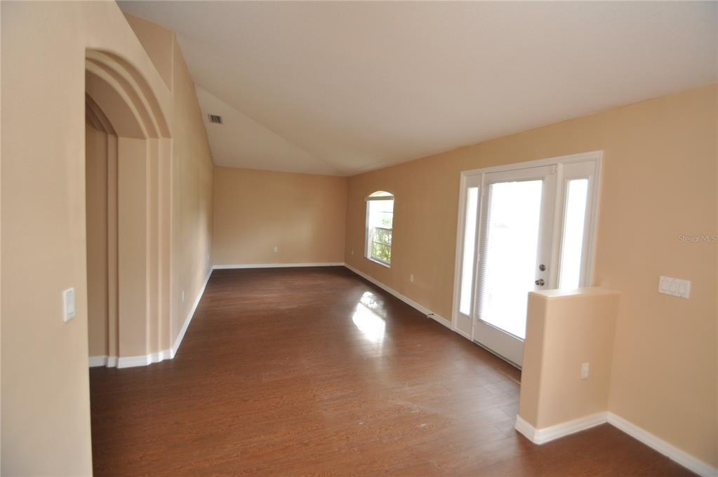 An empty room with vaulted ceilings, wood-look flooring, an arched entryway, and glass doors — 65 ROLLING FERN DRIVE, PALM COAST, FL