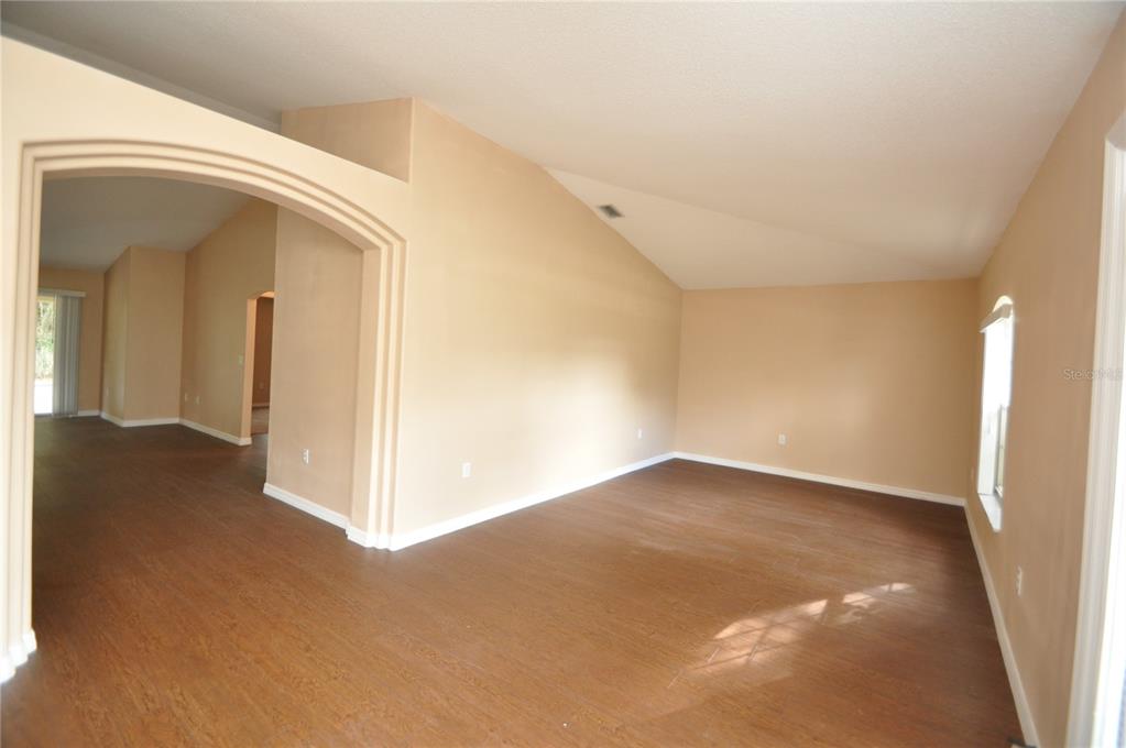 An empty room with vaulted ceilings, beige walls, and dark wood-look flooring — 65 ROLLING FERN DRIVE, PALM COAST, FL