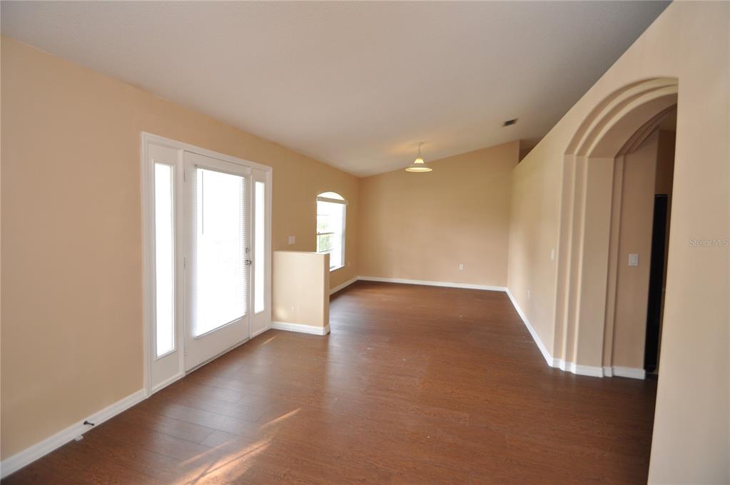 An empty room with wood-look flooring, beige walls, a vaulted ceiling, and an arched entryway — 65 ROLLING FERN DRIVE, PALM COAST, FL