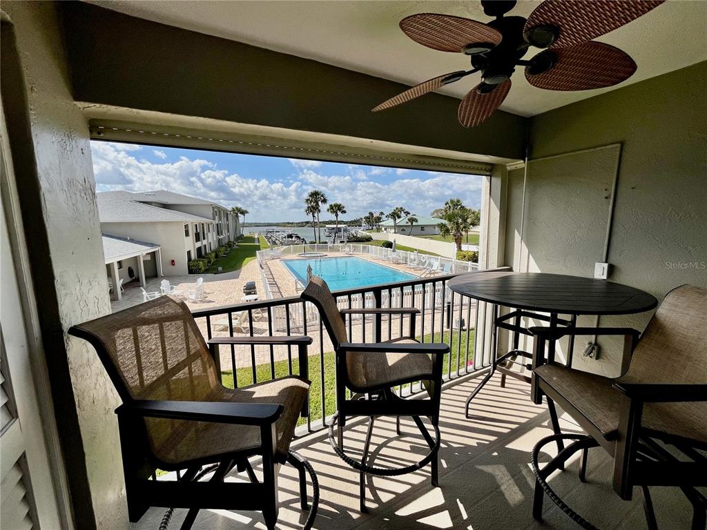 A covered balcony features patio furniture, a ceiling fan, and a view of a swimming pool — 2100 N PENINSULA AVENUE UNIT 216, NEW SMYRNA BEACH, FL