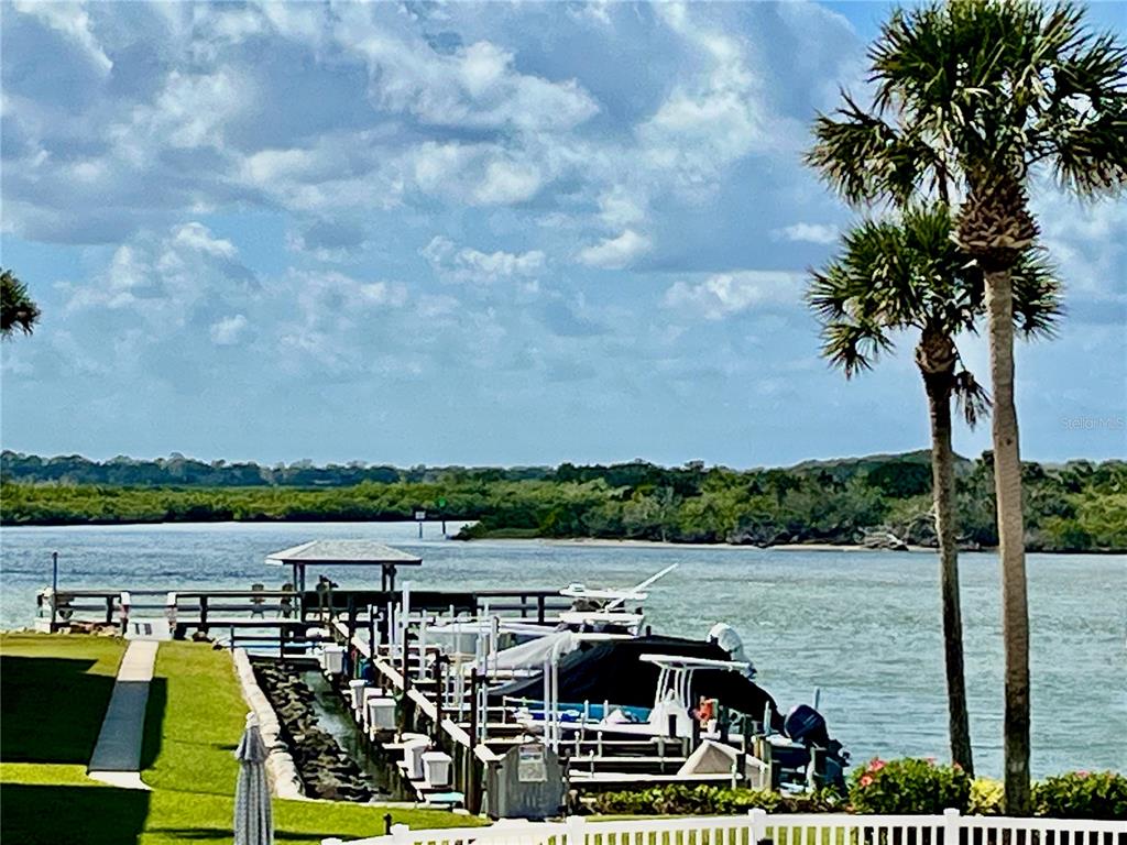 A wooden boat dock with covered slips extends into a waterway near palm trees — 2100 N PENINSULA AVENUE UNIT 216, NEW SMYRNA BEACH, FL