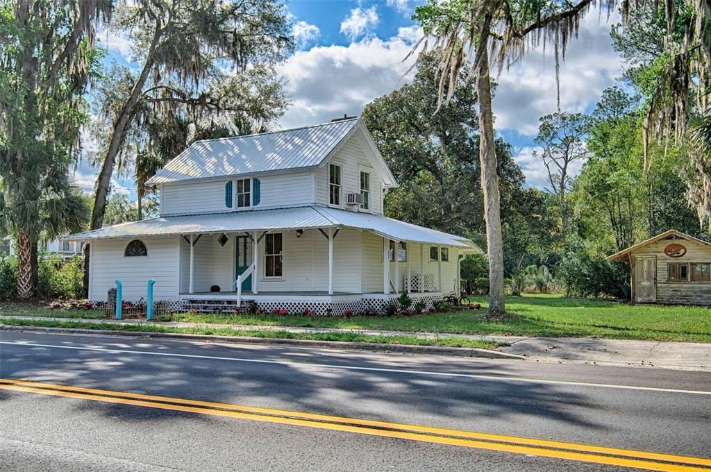 A white two-story house with a metal roof and wrap-around porch sits beside a road — 25415 NE STATE ROAD 26, MELROSE, FL