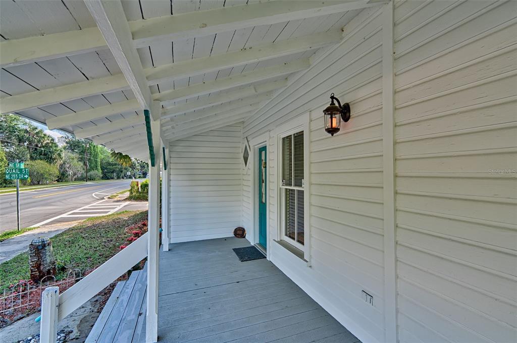 A white-sided house features a covered front porch with a teal door and wooden flooring — 25415 NE STATE ROAD 26, MELROSE, FL