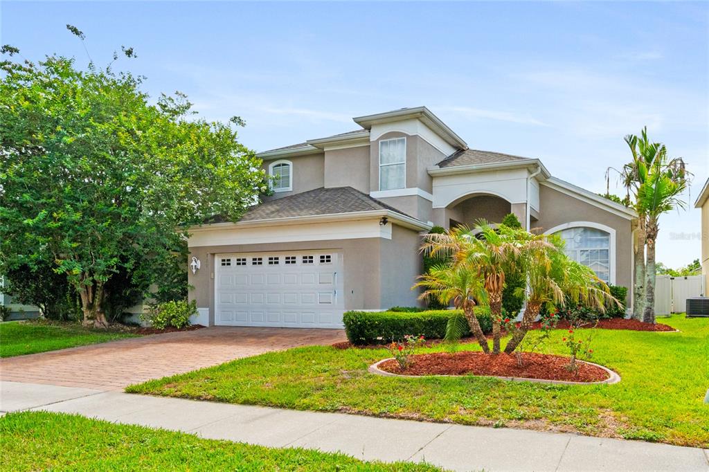 A two-story suburban house with a tan stucco exterior, a brick driveway, and a palm tree — 721 HARDWOOD CIRCLE, ORLANDO, FL