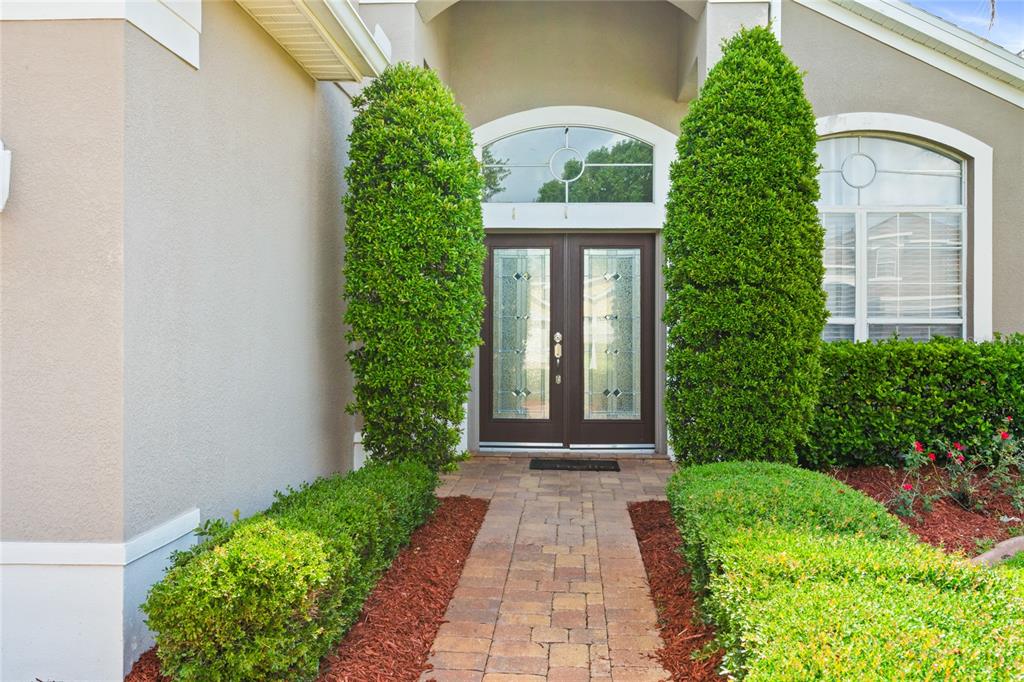 A paved walkway leads to a double front door flanked by tall, manicured shrubs — 721 HARDWOOD CIRCLE, ORLANDO, FL