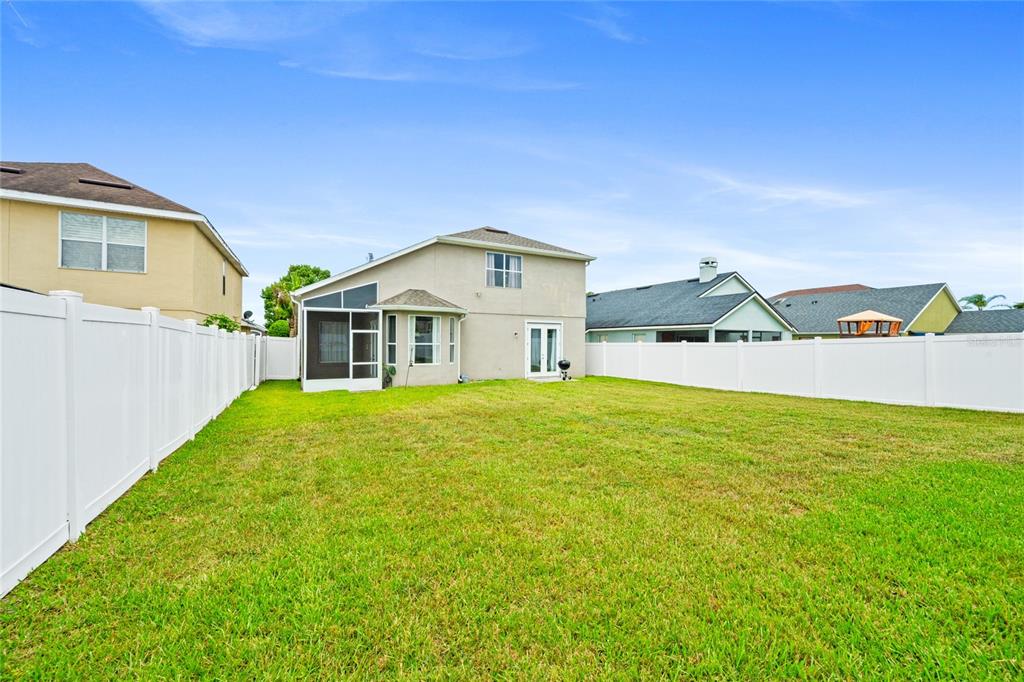 A backyard with a grassy lawn, a white vinyl fence, and a two-story house — 721 HARDWOOD CIRCLE, ORLANDO, FL