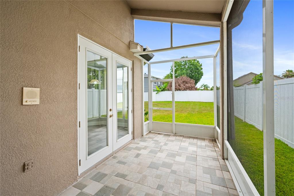A screened-in patio features tiled flooring, white French doors, and a view of the backyard — 721 HARDWOOD CIRCLE, ORLANDO, FL