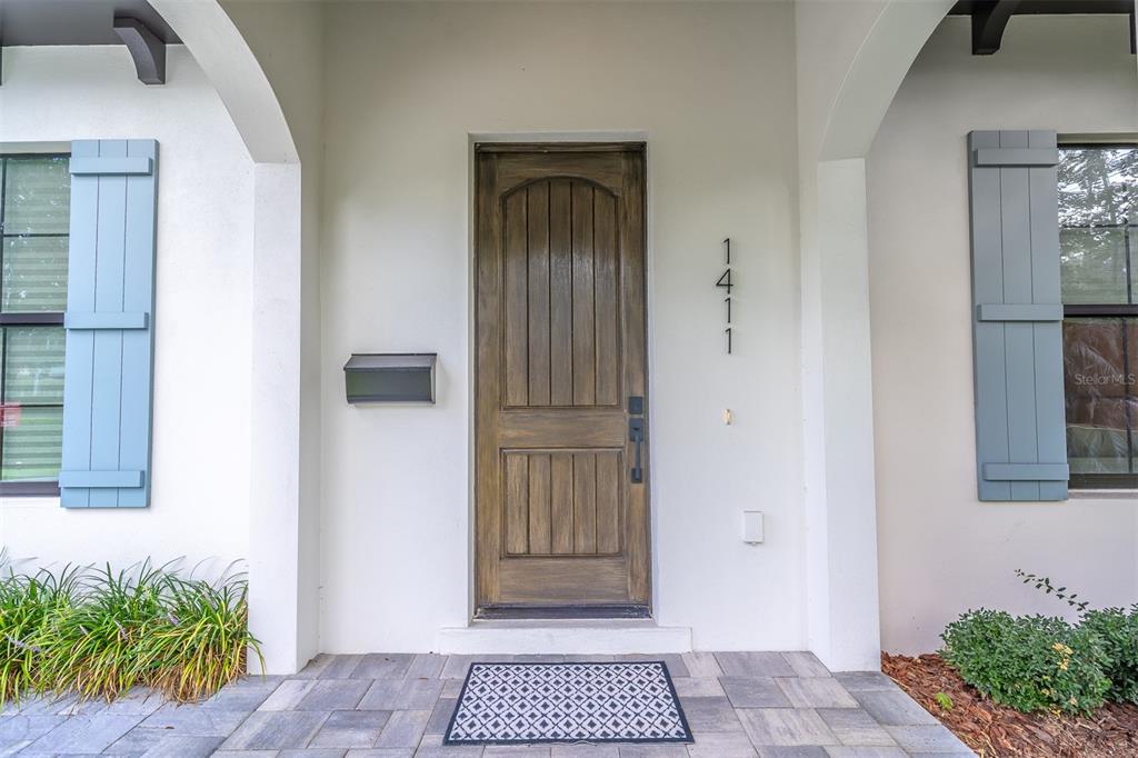 A wooden front door with a mailbox is centered between two windows with blue shutters — 1411 MILLER AVENUE, WINTER PARK, FL