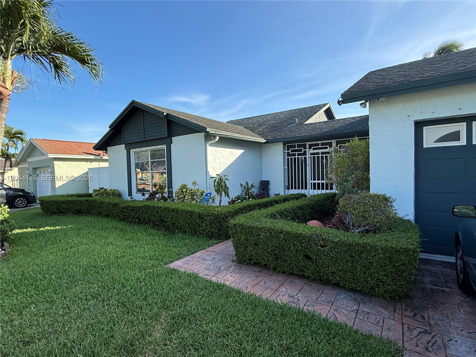 A single-story house features a white stucco exterior, dark trim, and a manicured hedge — 15622 SW 142nd Ct, Miami FL 33177, MIAMI, FL