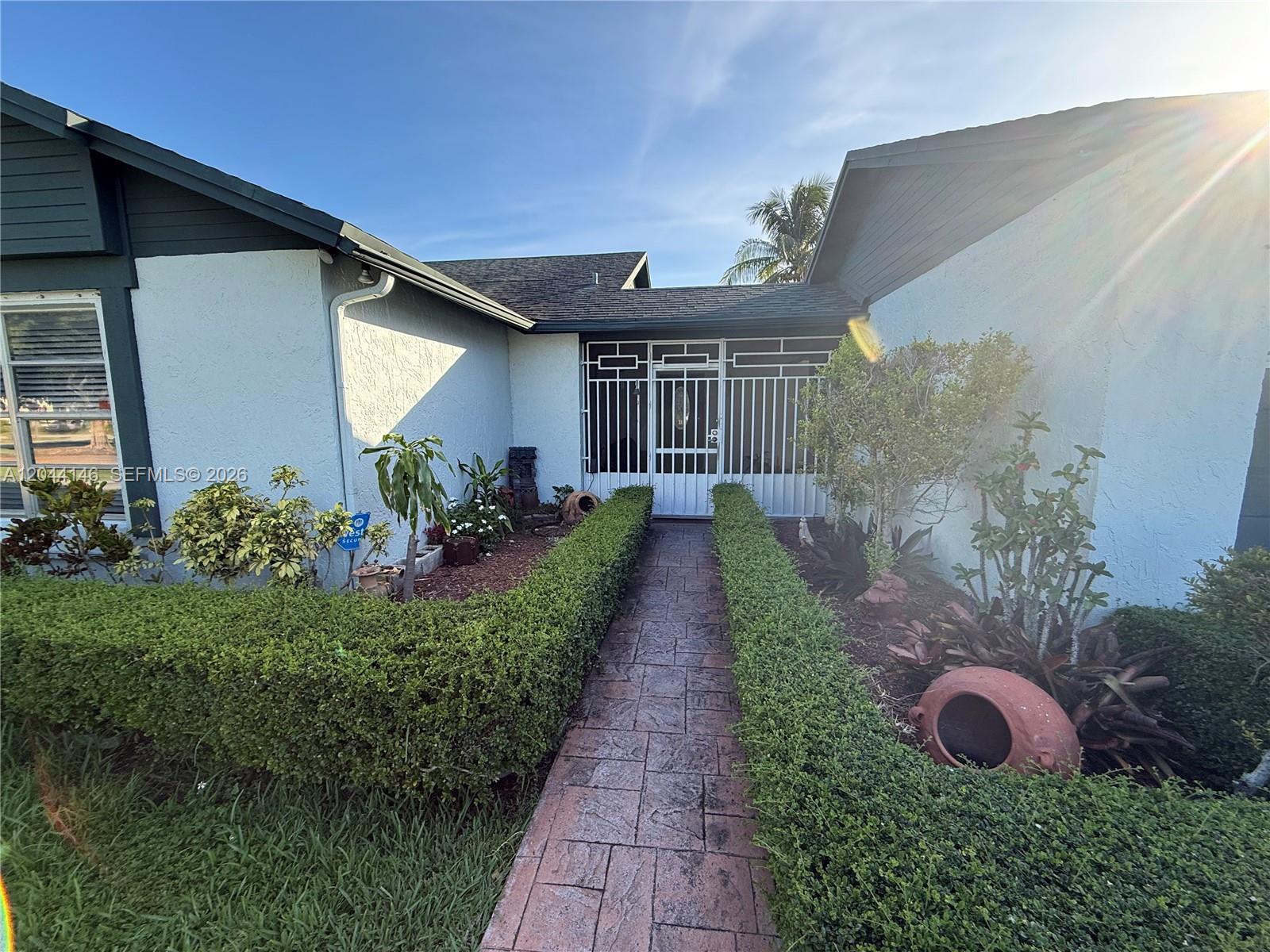 A stone walkway leads to a white metal security gate at the home's entrance — 15622 SW 142nd Ct, Miami FL 33177, MIAMI, FL