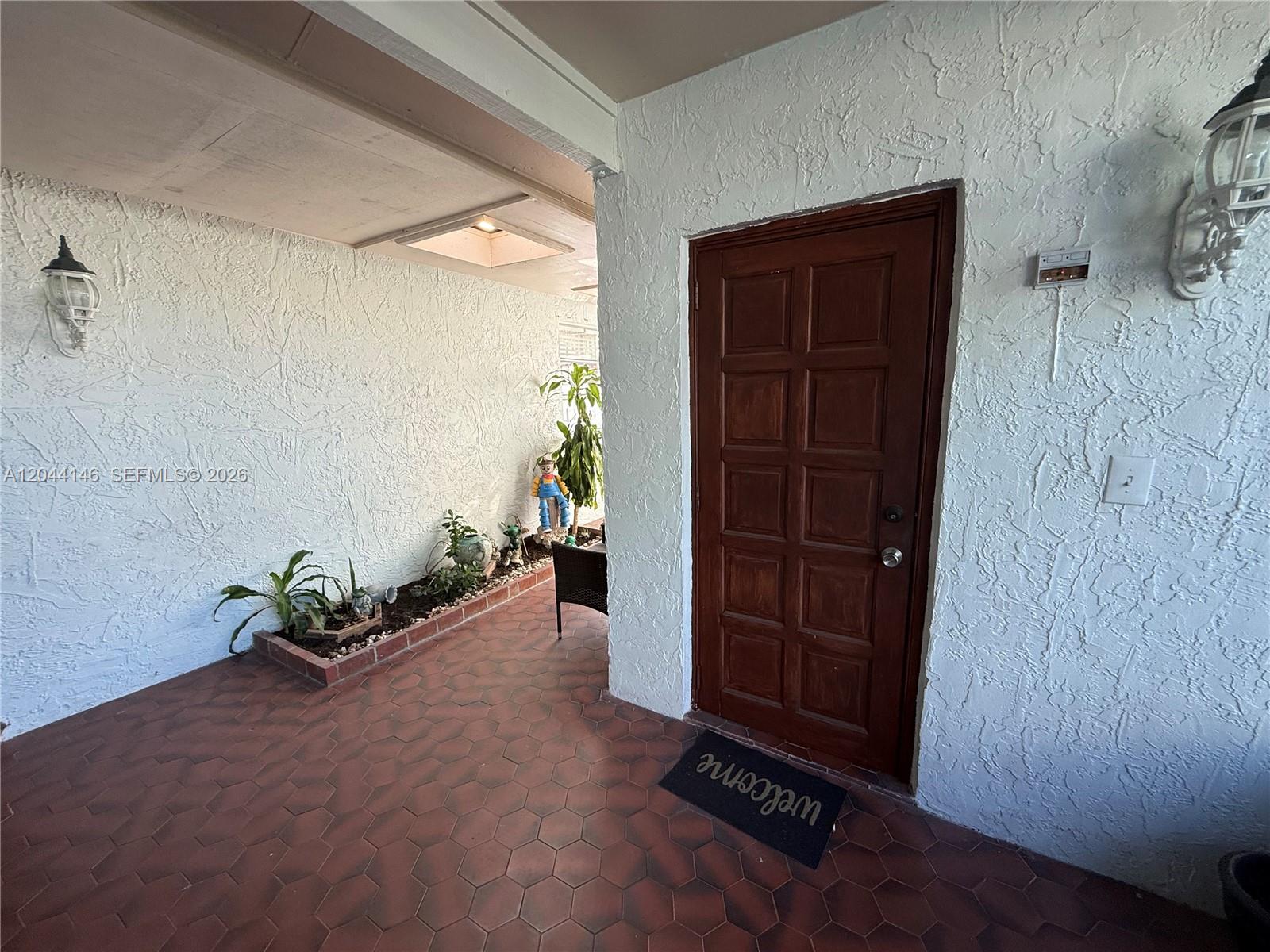 A covered porch features a wooden door, textured white walls, and hexagonal floor tiles — 15622 SW 142nd Ct, Miami FL 33177, MIAMI, FL