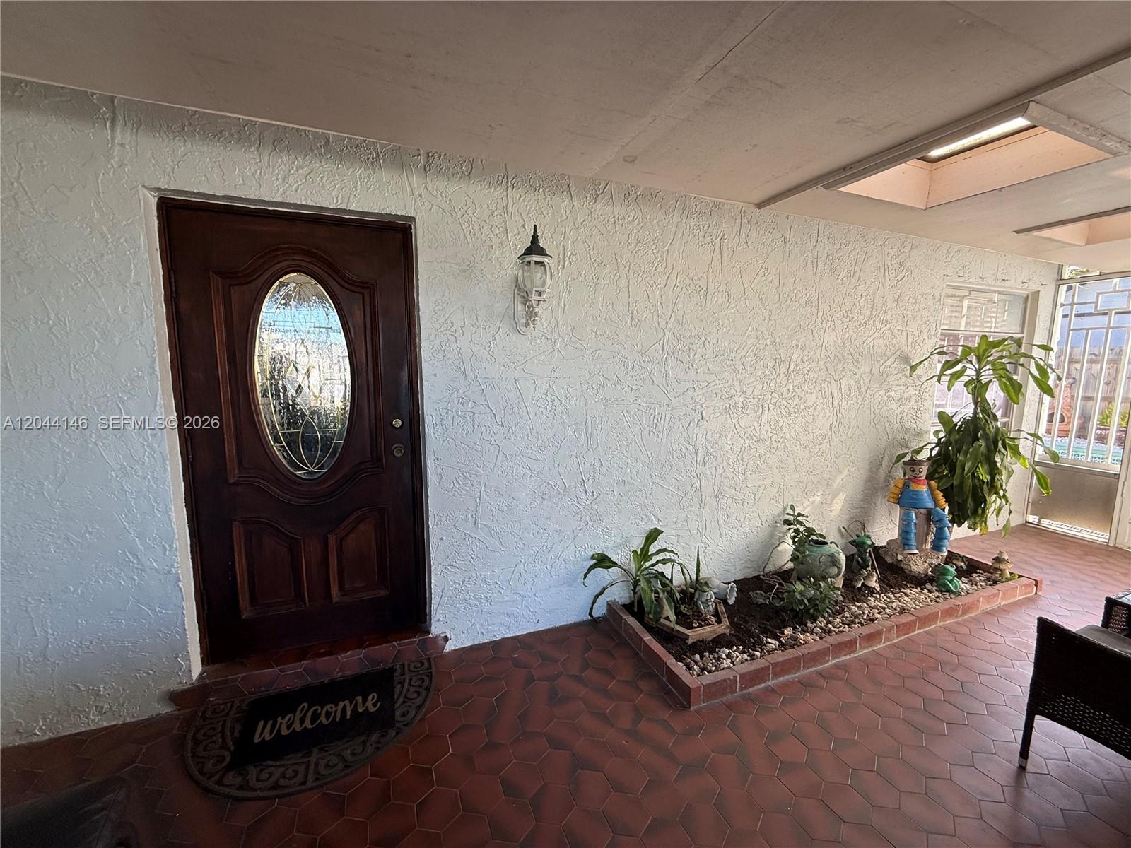 A covered entryway features a dark wood door, textured white walls, and a brick planter — 15622 SW 142nd Ct, Miami FL 33177, MIAMI, FL