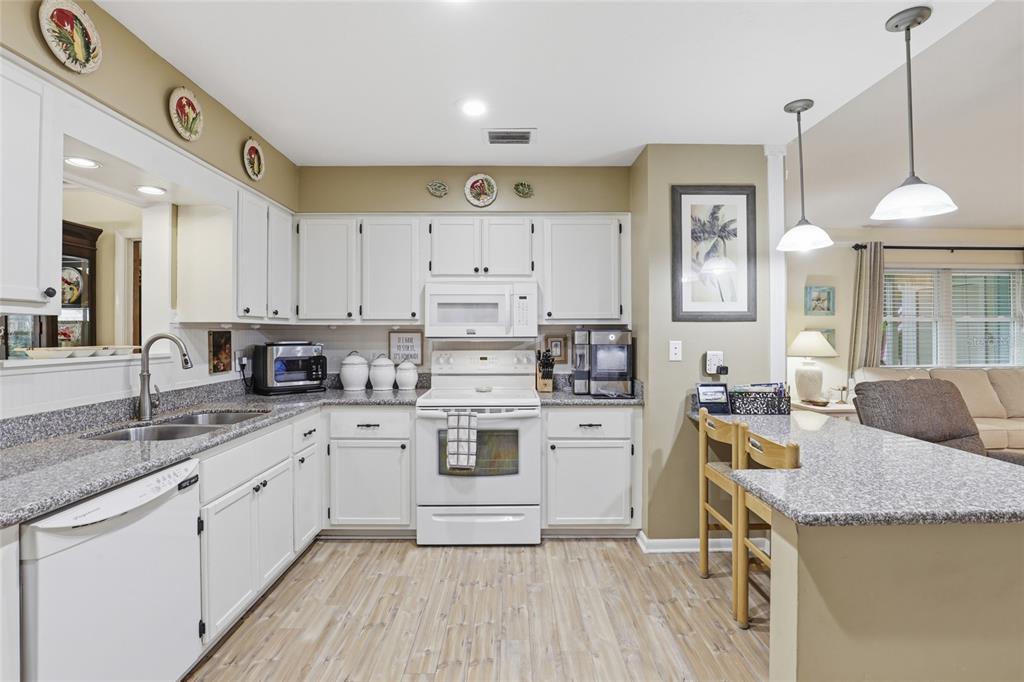 A kitchen with white cabinets, granite countertops, stainless steel appliances, and a breakfast bar — 710 SW 77TH TERRACE, GAINESVILLE, FL