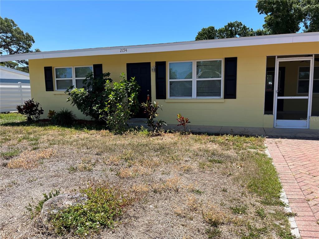A yellow single-story house features a front door, windows with black shutters, and a walkway — 2154 INNER CASS CIRCLE, SARASOTA, FL
