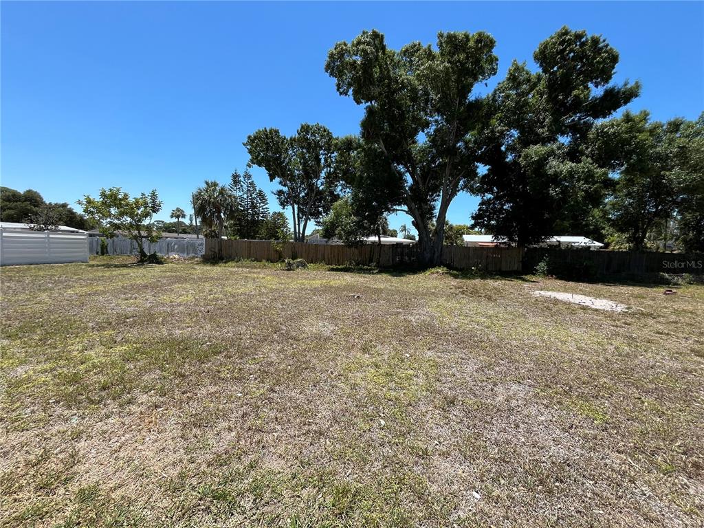 A vacant, grassy lot features a wooden fence and several large trees under a blue sky — 2154 INNER CASS CIRCLE, SARASOTA, FL
