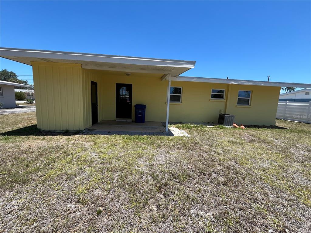 The exterior of a yellow house features a covered patio, a dark door, and windows — 2154 INNER CASS CIRCLE, SARASOTA, FL