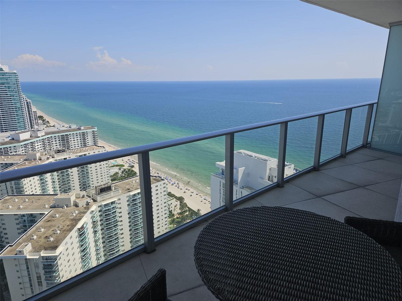 A balcony with a round table overlooks a beach, the ocean, and nearby high-rise buildings — 4111 S Ocean Dr # 3308, Hollywood FL 33019, HOLLYWOOD, FL