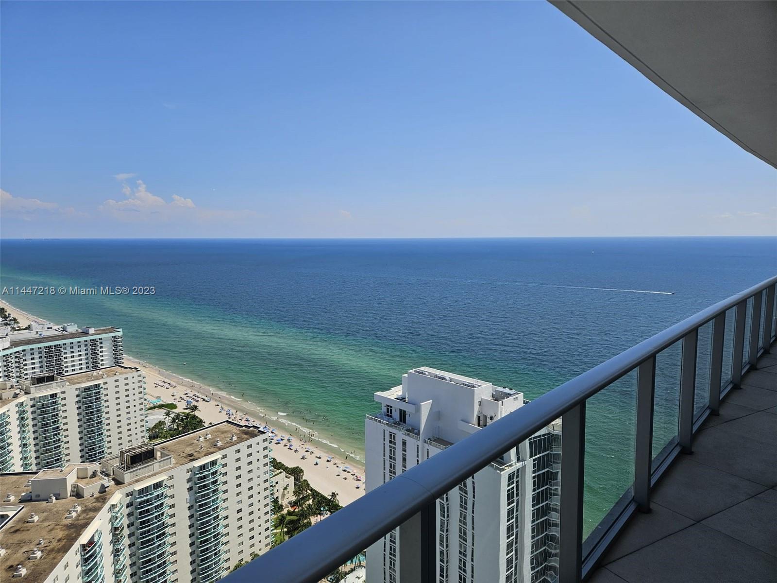 A high-rise balcony overlooks a sandy beach and the ocean under a clear sky — 4111 S Ocean Dr # 3308, Hollywood FL 33019, HOLLYWOOD, FL