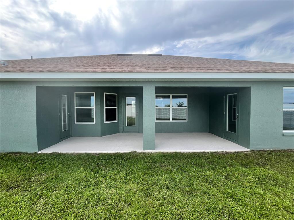 A covered concrete patio sits at the rear of a house with green exterior walls — 16794 SE 23RD AVENUE, SUMMERFIELD, FL