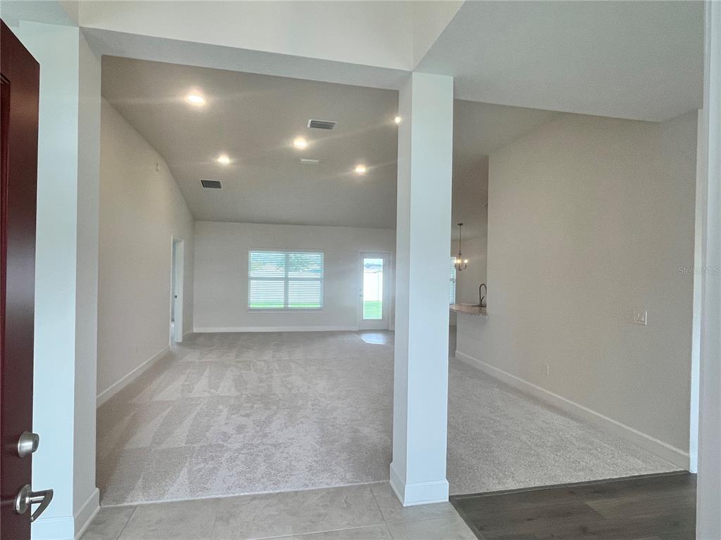 A view from a tiled entryway looking into a carpeted living area with vaulted ceilings — 16794 SE 23RD AVENUE, SUMMERFIELD, FL