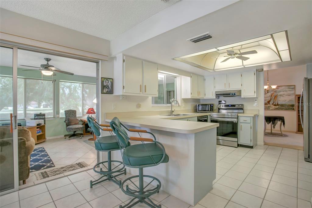 A kitchen with white cabinets and a breakfast bar overlooks an adjacent sunroom — 5817 11TH AVENUE W, BRADENTON, FL
