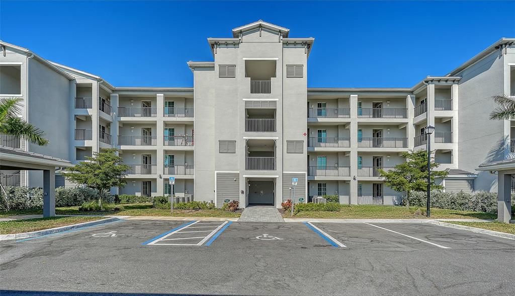 A multi-story apartment building exterior with a central entrance and accessible parking spaces in front — 12180 WELLEN GOLF STREET UNIT 308, VENICE, FL
