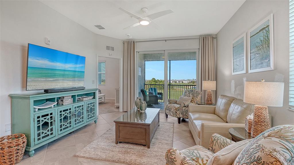 A living room features a television on a teal console, a sofa, and sliding glass doors — 12180 WELLEN GOLF STREET UNIT 308, VENICE, FL