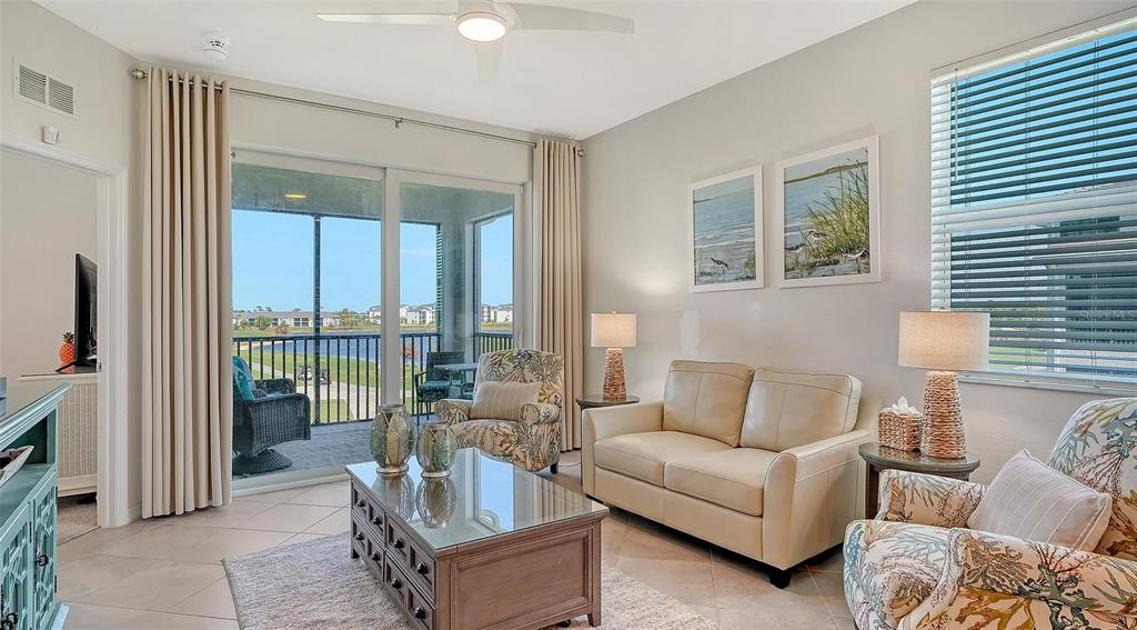 A living room features a beige sofa, patterned armchairs, a glass-topped coffee table, and balcony access — 12180 WELLEN GOLF STREET UNIT 308, VENICE, FL