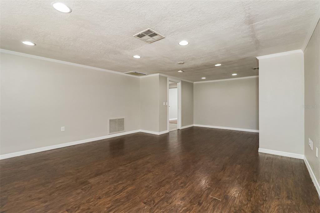 A spacious room features light gray walls, recessed ceiling lights, and dark wood-look flooring — 3644 PANOLA DRIVE, NEW PORT RICHEY, FL