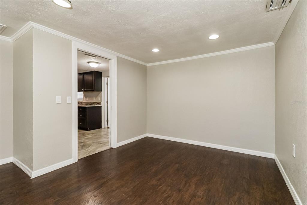 A room with dark wood flooring, light gray walls, and a doorway leading to a kitchen — 3644 PANOLA DRIVE, NEW PORT RICHEY, FL