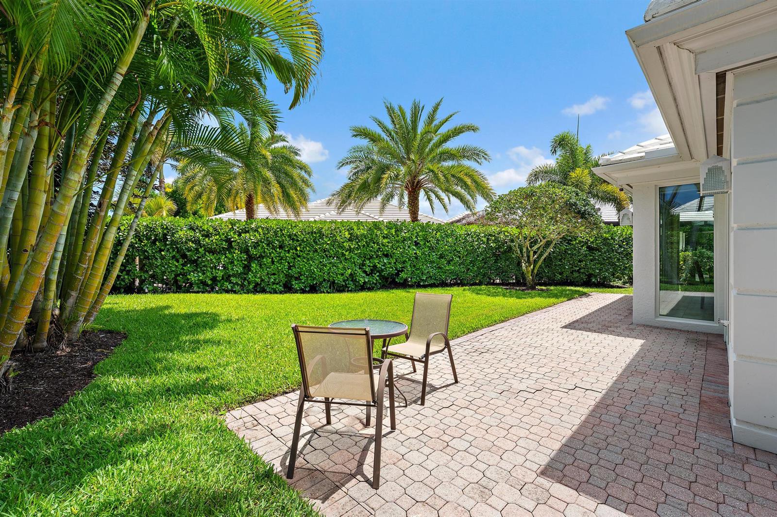 A patio with a small table and two chairs sits beside a house with landscaping — 4501 Captains Way, Jupiter FL 33477, JUPITER, FL