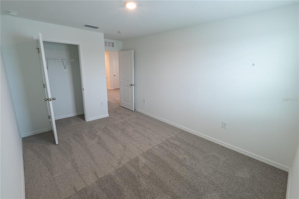 An empty bedroom features gray carpeting, white walls, a closet, and an open doorway — 4409 SAND DOLLAR WAY, ZEPHYRHILLS, FL