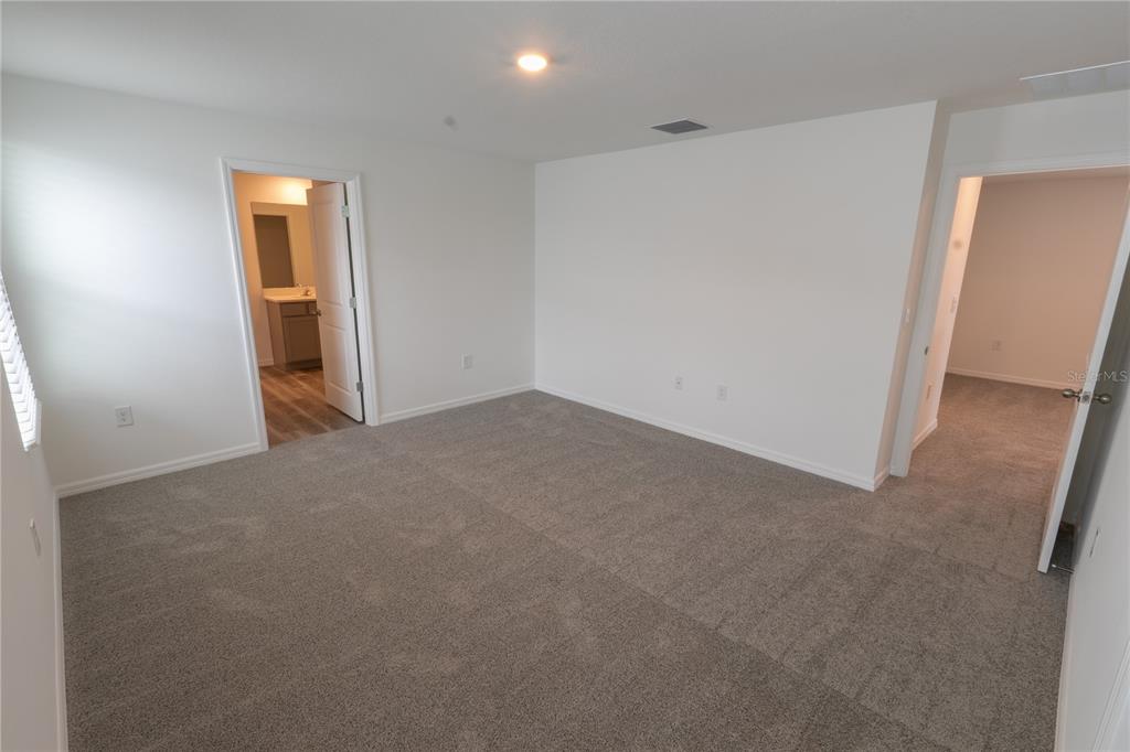 An empty bedroom features gray carpeting, white walls, and two doorways leading to other rooms — 4409 SAND DOLLAR WAY, ZEPHYRHILLS, FL