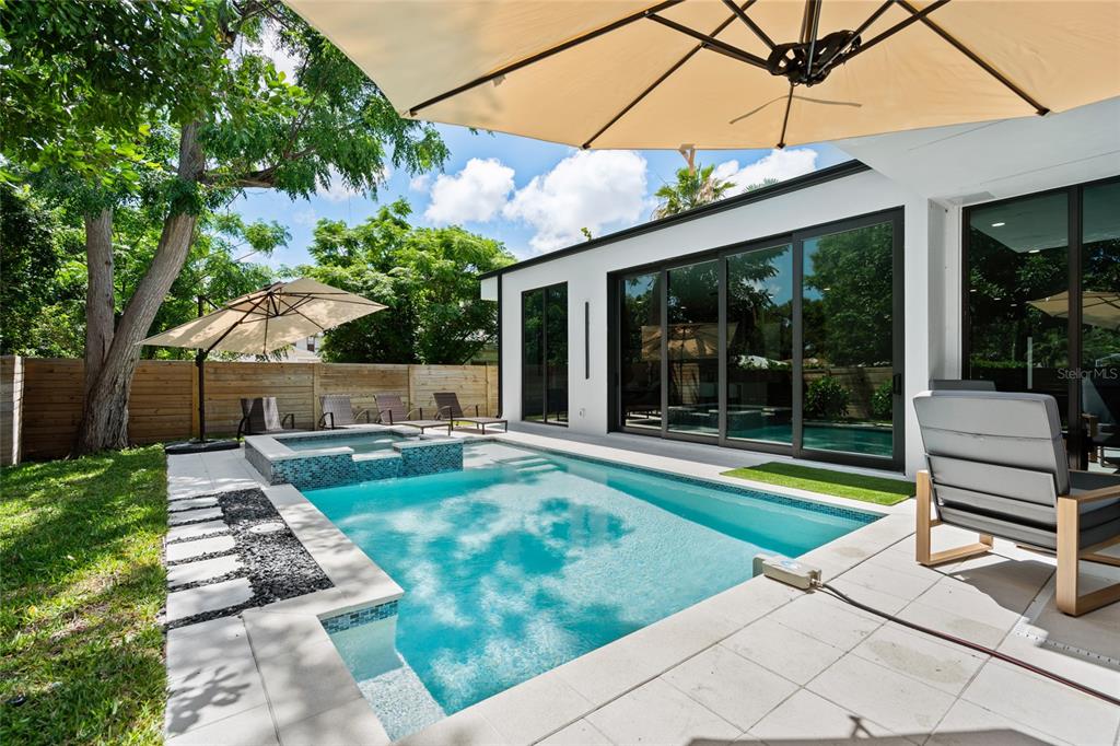 A modern backyard features a swimming pool with an integrated spa and a patio area — 2441 WEBBER STREET, SARASOTA, FL
