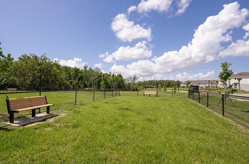 A fenced-in grassy dog park features two benches under a bright blue sky — 2707 GINGER LANE, HAINES CITY, FL