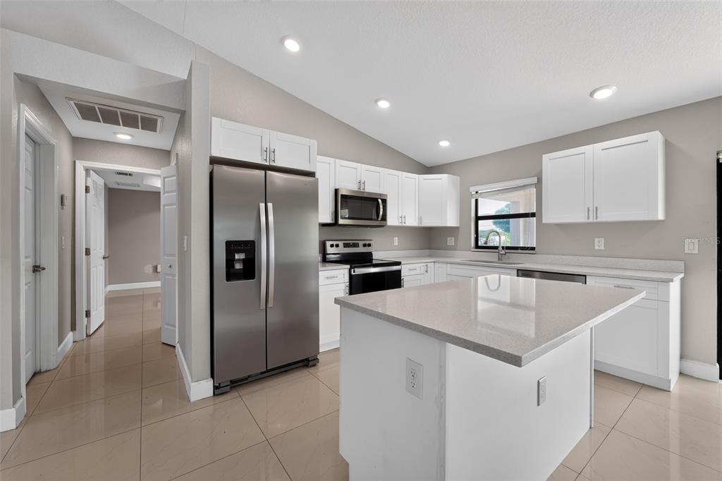 A modern kitchen features white cabinets, stainless steel appliances, a center island, and tile flooring — 2712 15TH STREET SW, LEHIGH ACRES, FL