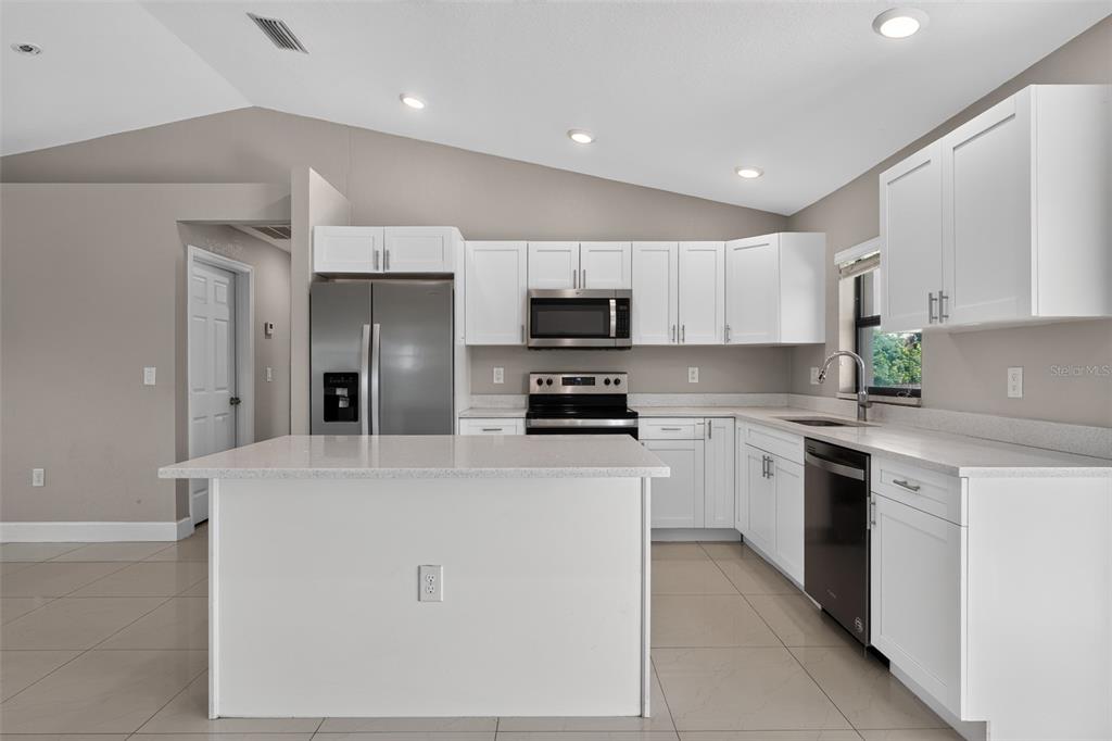 A kitchen with white cabinets, stainless steel appliances, a center island, and tile flooring — 2712 15TH STREET SW, LEHIGH ACRES, FL