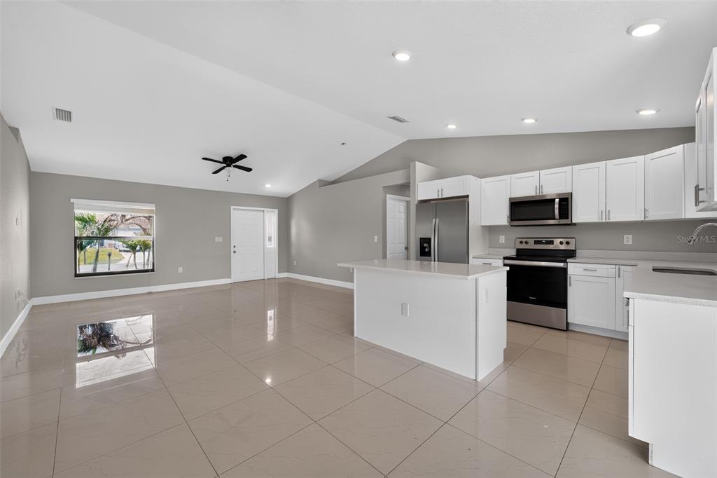 An open-concept kitchen and living area features white cabinetry, stainless steel appliances, and tile flooring — 2712 15TH STREET SW, LEHIGH ACRES, FL