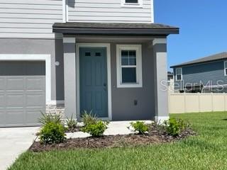 A gray house exterior features a blue front door, a garage, and a small garden — 3314 FRESNO PL, ZEPHYRHILLS, FL