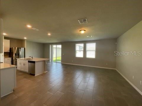 An open-concept kitchen and living area with tile flooring, white cabinets, and stainless appliances — 3314 FRESNO PL, ZEPHYRHILLS, FL