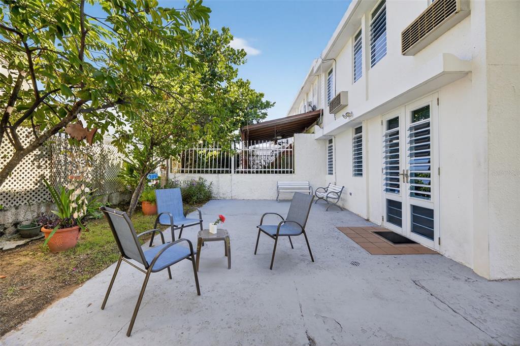 A concrete patio with outdoor furniture sits beside a white building with louvered glass doors — D-1-20 CALLE CAMBIJA, RINCON, PR