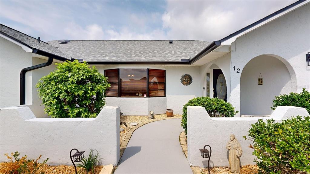 A white stucco house exterior features a gray shingled roof and a paved walkway entrance — 12 CLASSIC COURT S, PALM COAST, FL