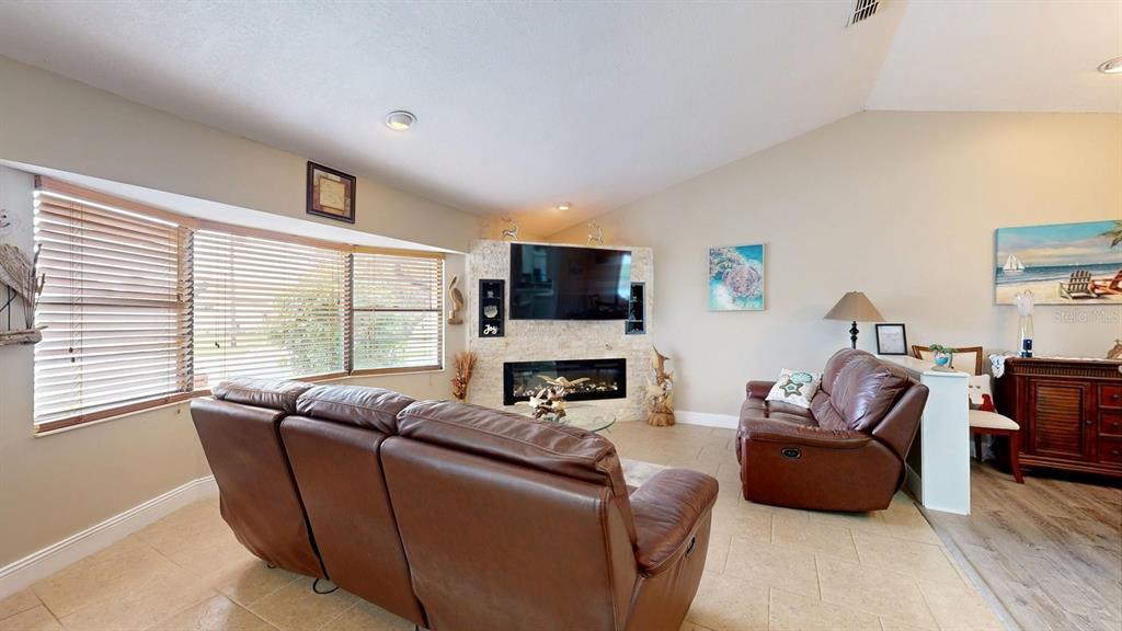 A living room features a stone fireplace, a wall-mounted television, and brown leather furniture — 12 CLASSIC COURT S, PALM COAST, FL