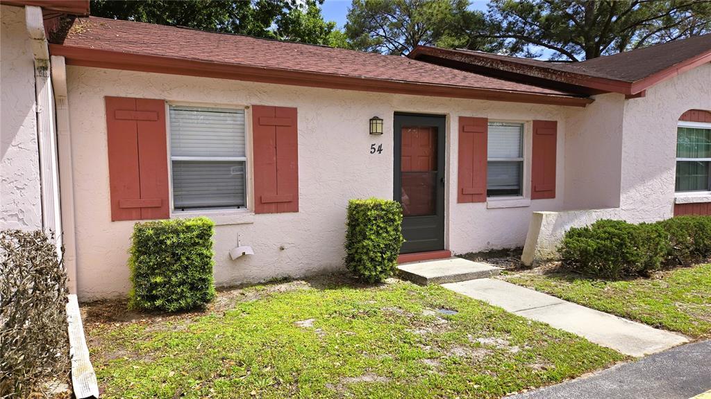 A single-story stucco house features a front door, two windows with red shutters, and landscaping — 54 W MARBRISA WAY, KISSIMMEE, FL